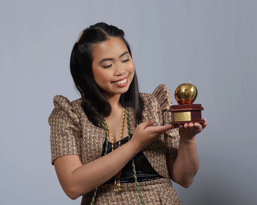 Woman in a brown dress holding a golden trophy in her hands, smiling and looking at the camera.