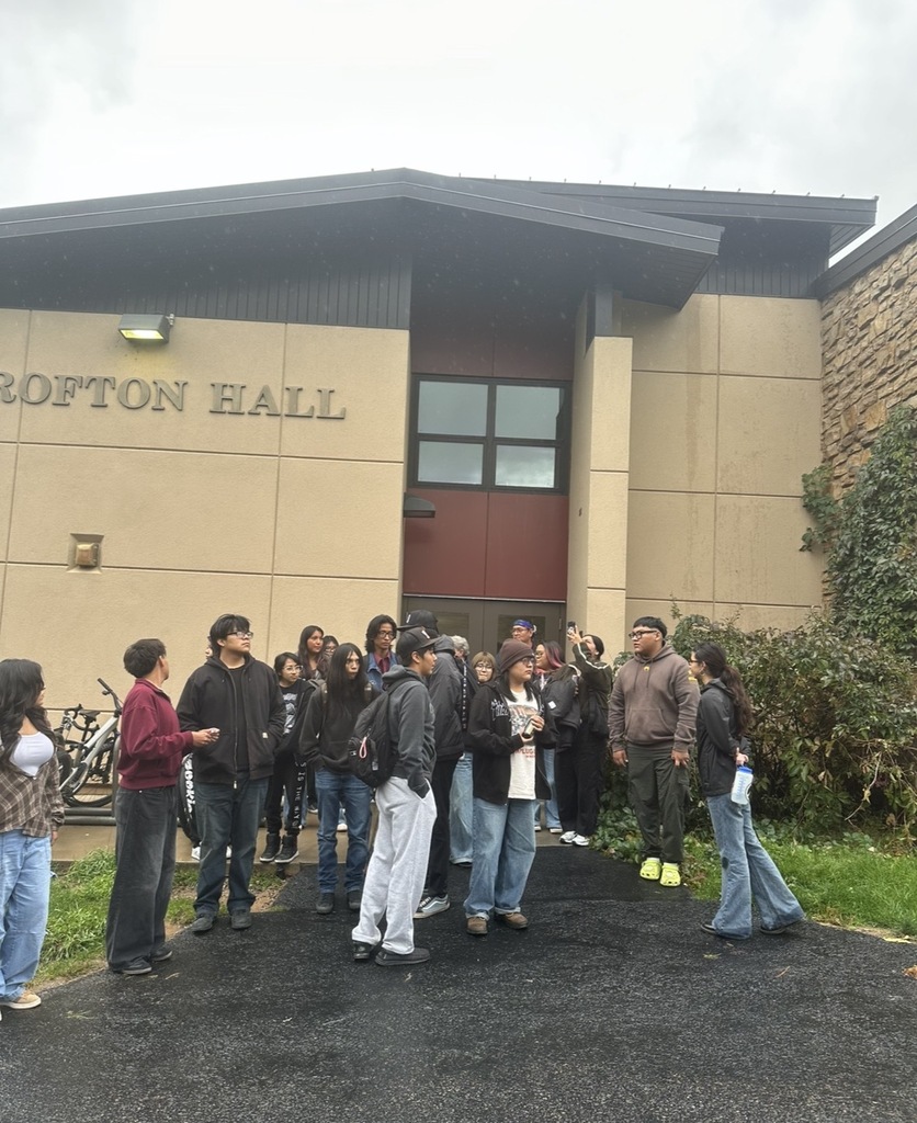 Multiple people in front of a building with text that reads "Rofton Hall". Some people carry bags.