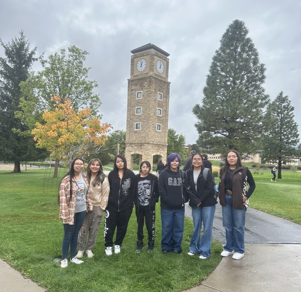 A group of six people stands in a park with a clock tower and trees.