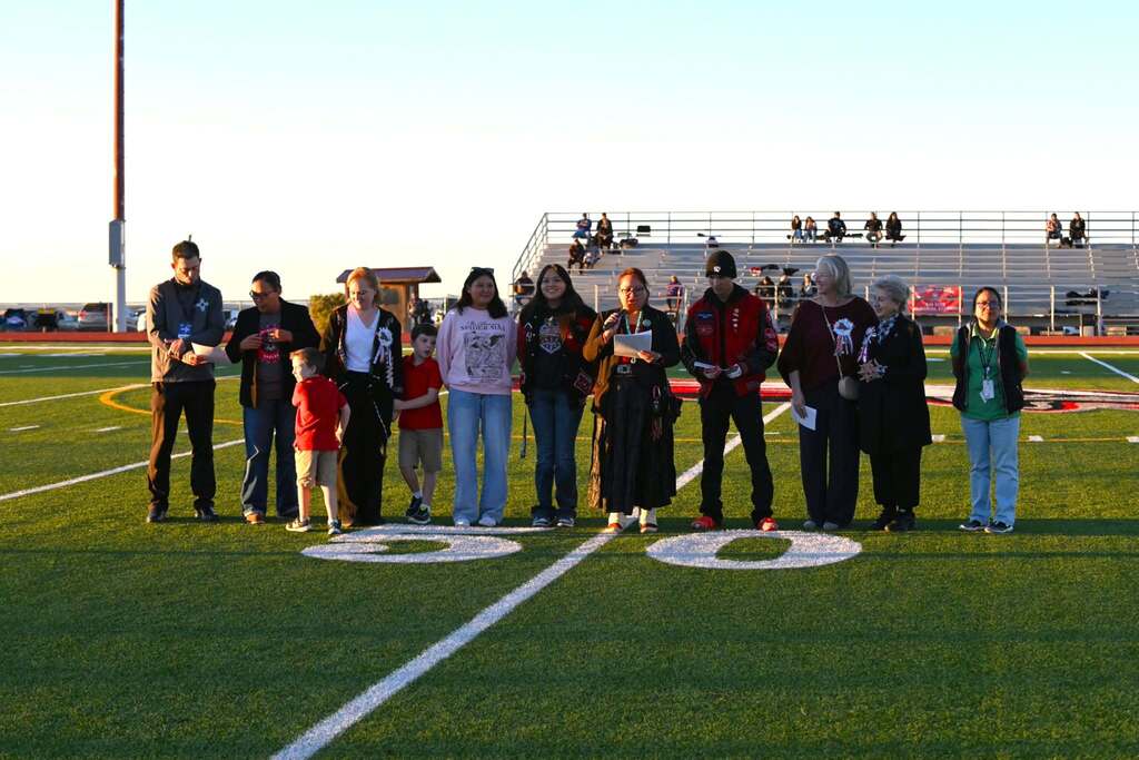 A group of people standing on a field with numbers "50" painted, bleachers in the background.