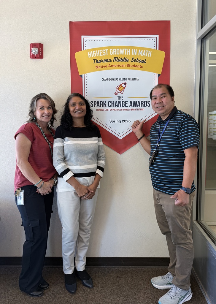 Three adults stand in front of a wall with a banner behind them. A red banner reads "Highest Growth in Math."
