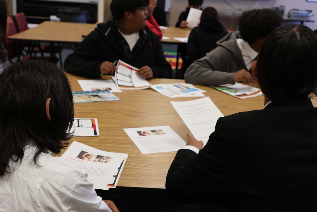 Several students seated around a table, each holding papers and engaged in a discussion.