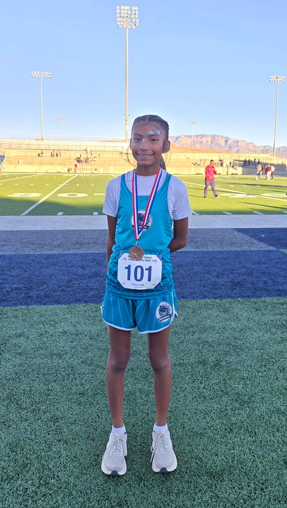 A young person stands on a field with a medal around their neck. Number 101 is on their shirt.