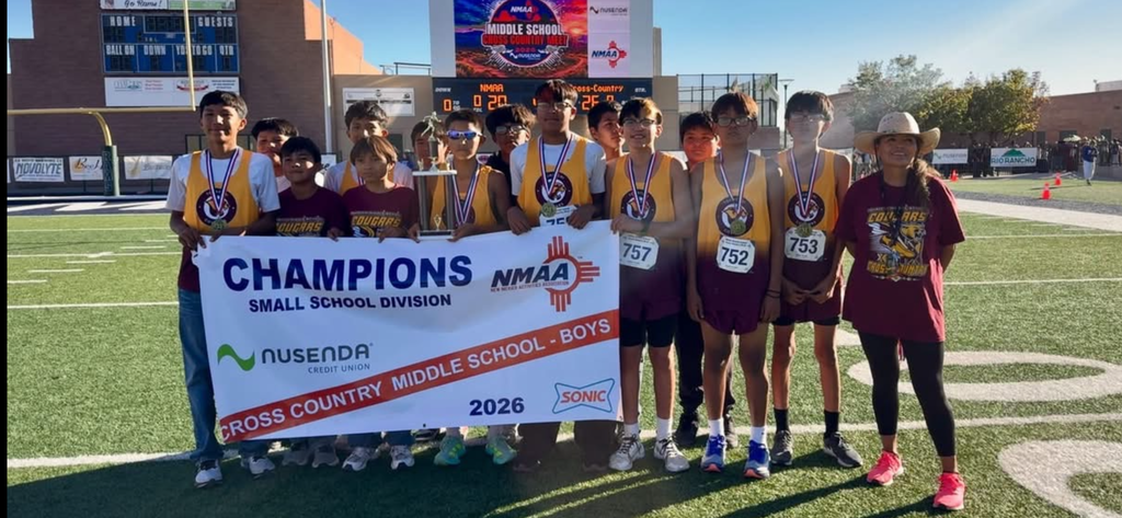 Group of boys pose with banner that reads "CHAMPIONS" and "CROSS COUNTRY MIDDLE SCHOOL BOYS" on field.