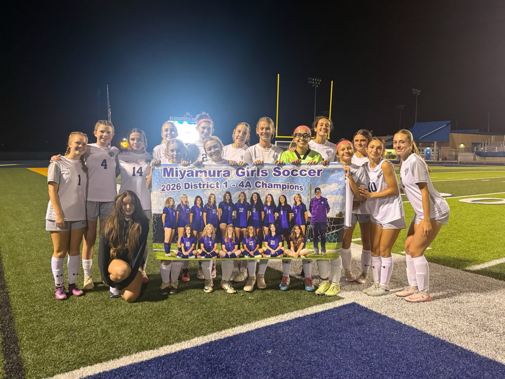 A group of girls' soccer players pose with a banner on a field at night.