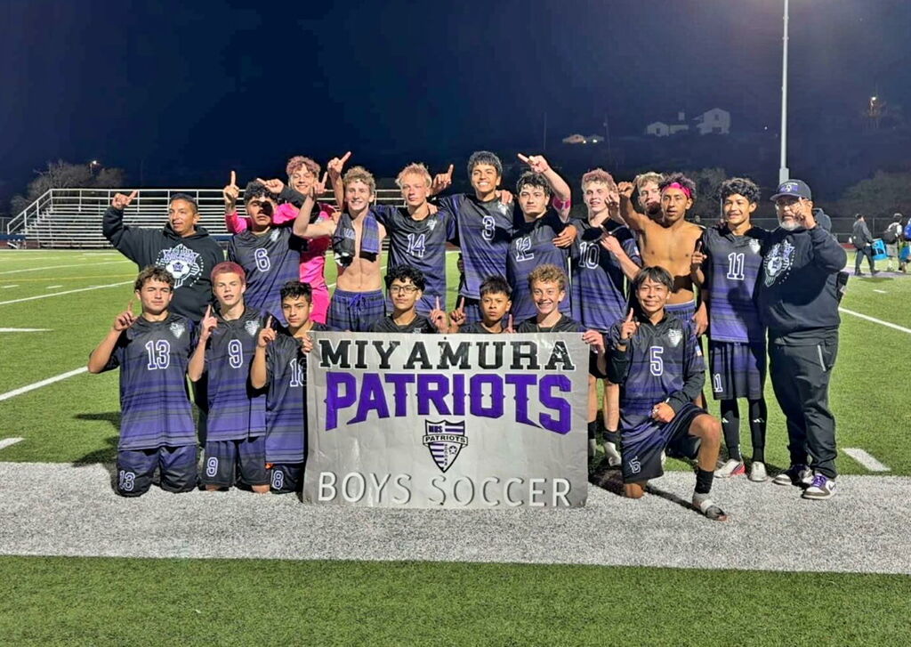 A sports team poses for a photo in front of a sign with a large "Patriots" logo.