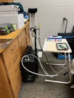 Small room with a table, drawers, and a computer on it. Cables are attached to the computer.