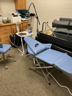 Interior of a room with blue reclining chairs, a small table, a wooden desk, and a printer.