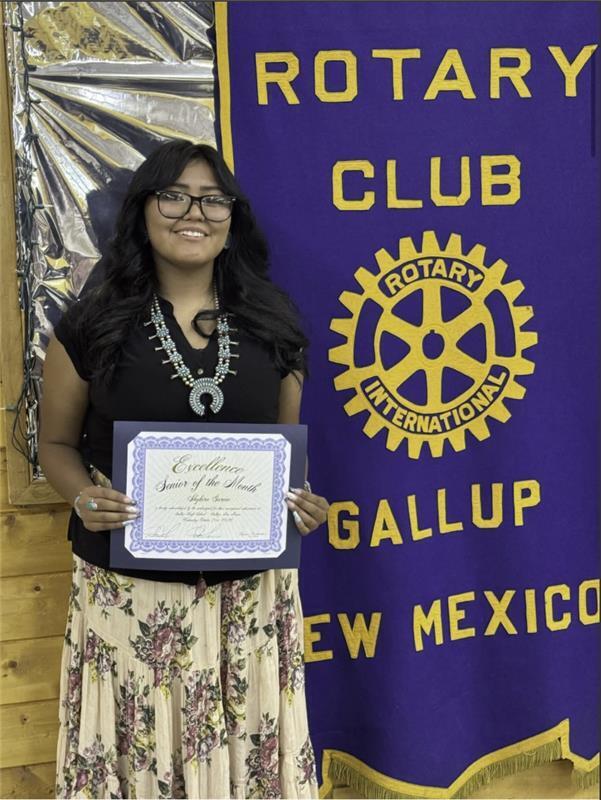Person holding certificate in front of banner with text Rotary Club Gallup New Mexico.