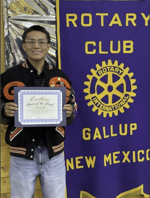 Man holds certificate in front of banner reading "Rotary Club Gallup New Mexico".
