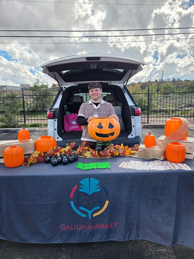 Person holds pumpkin on table covered with pumpkins and fall decorations in front of SUV.