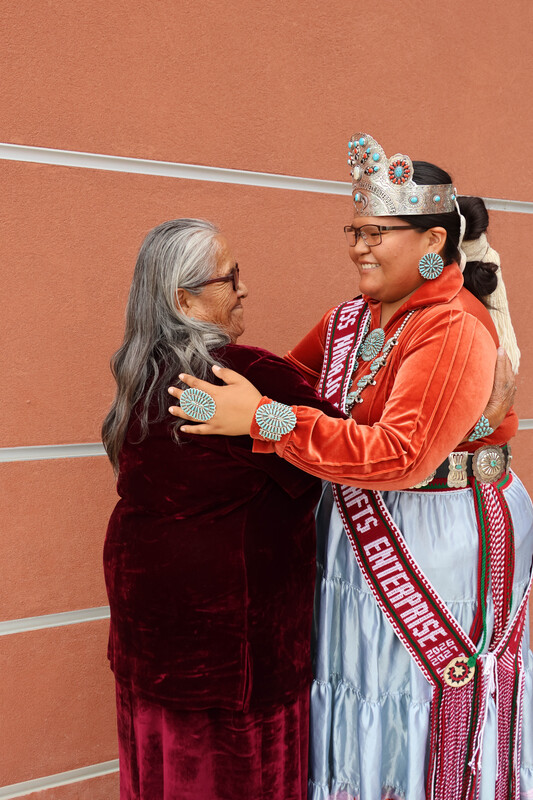 two women embracing, one wearing traditional Navajo clothing and jewelry