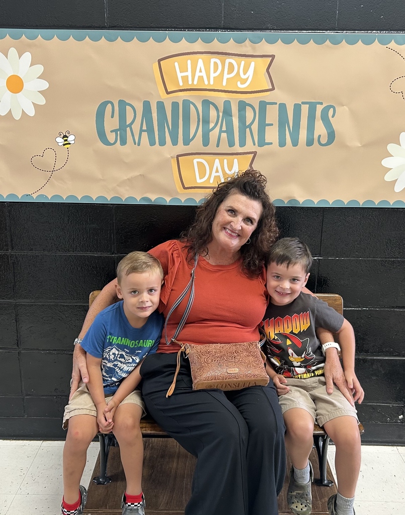 Two children sit with a grandparent beneath the Happy Grandparents Day banner.