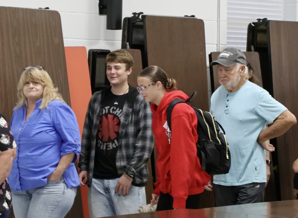 Two students stand with two grandparents in the school cafeteria during Grandparents’ Day.