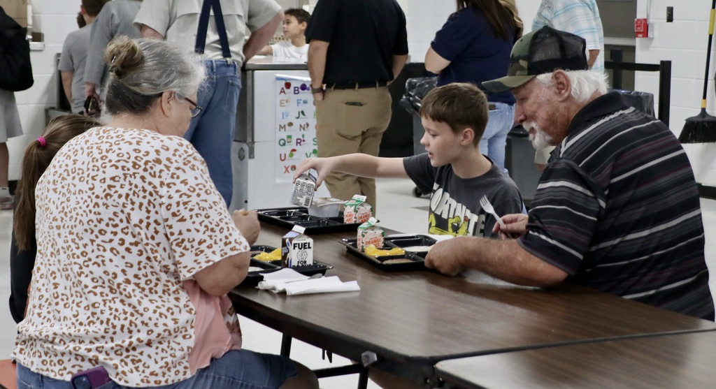 A student and grandparents share breakfast at a cafeteria table.