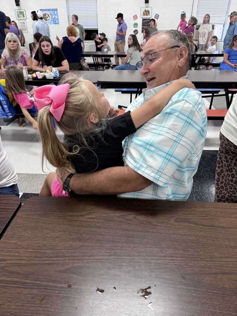A student hugs a grandparent at a cafeteria table during Grandparents’ Day.
