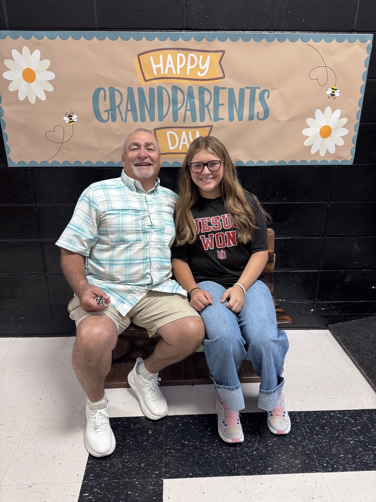 A student and grandparent smile together beneath the Happy Grandparents Day banner.