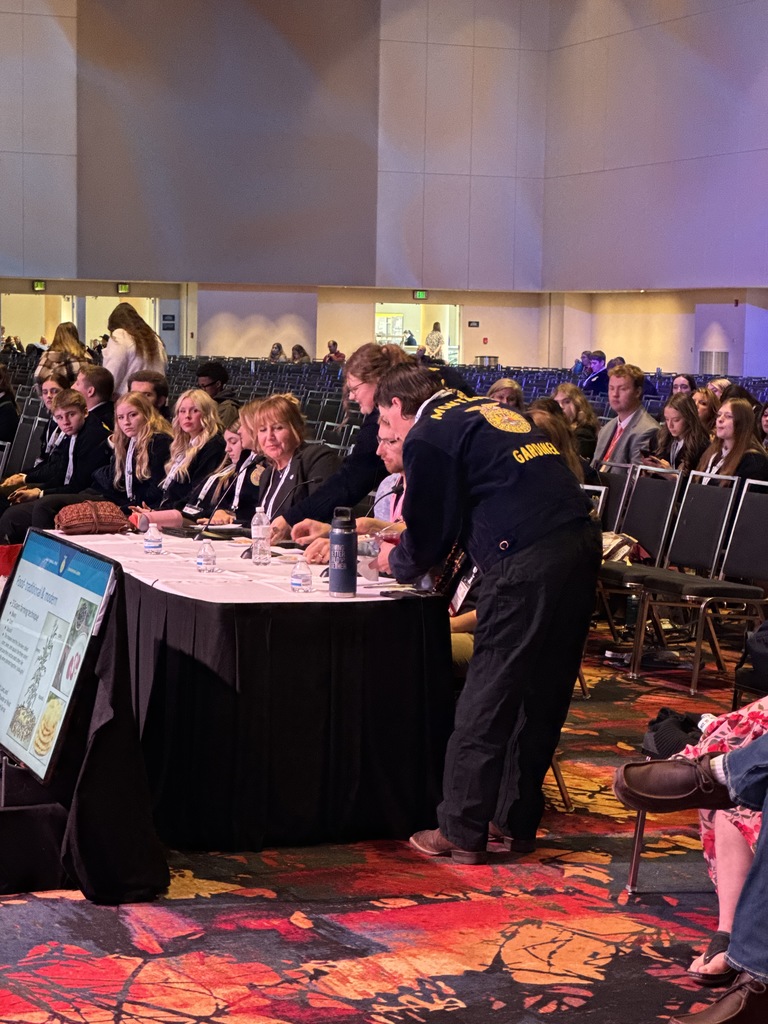 Two FFA members are serving a sample of food to the judges while they are seated at a table.