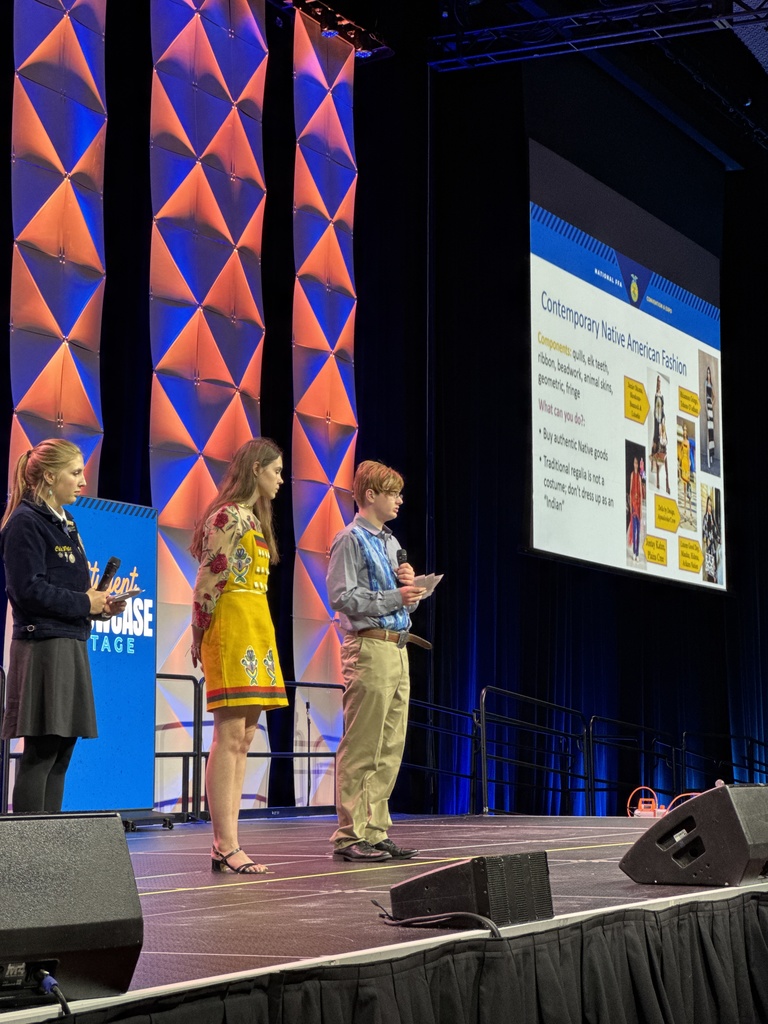 The three FFA members presenting on the stage at National FFA Convention are seen from the side with th e projected slideshow seen in the background.