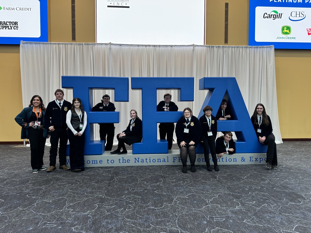 Ten FFA members and FFA advisor pose by large blue letters that spell FFA at the national FFA convention.