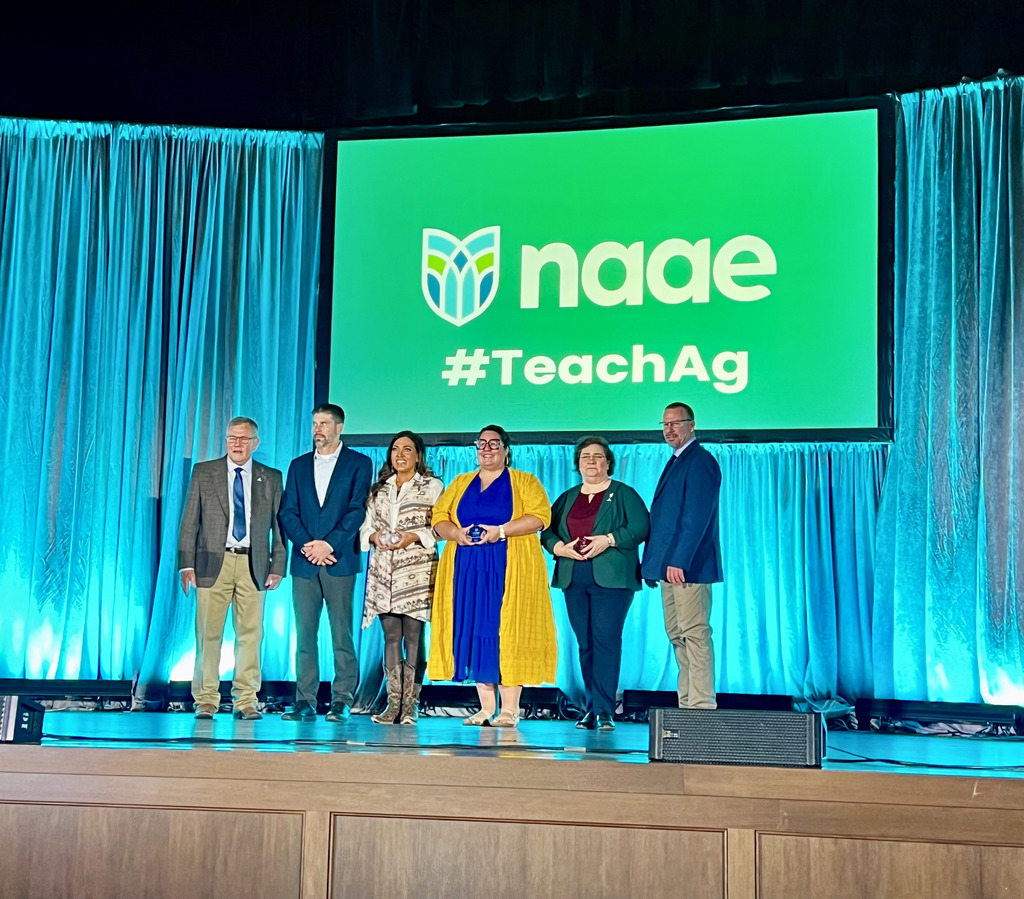 Lori Hoppe stands on stage at the NAAE Convention along with three other teachers a part of the INFLUENCE program as well as outgoing and incoming NAAE presidents.