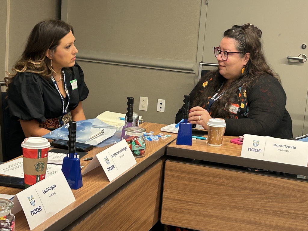 Lori Hoppe, seated at a table, listens to fellow agriculture teacher as they work during their INFLUENCE program.