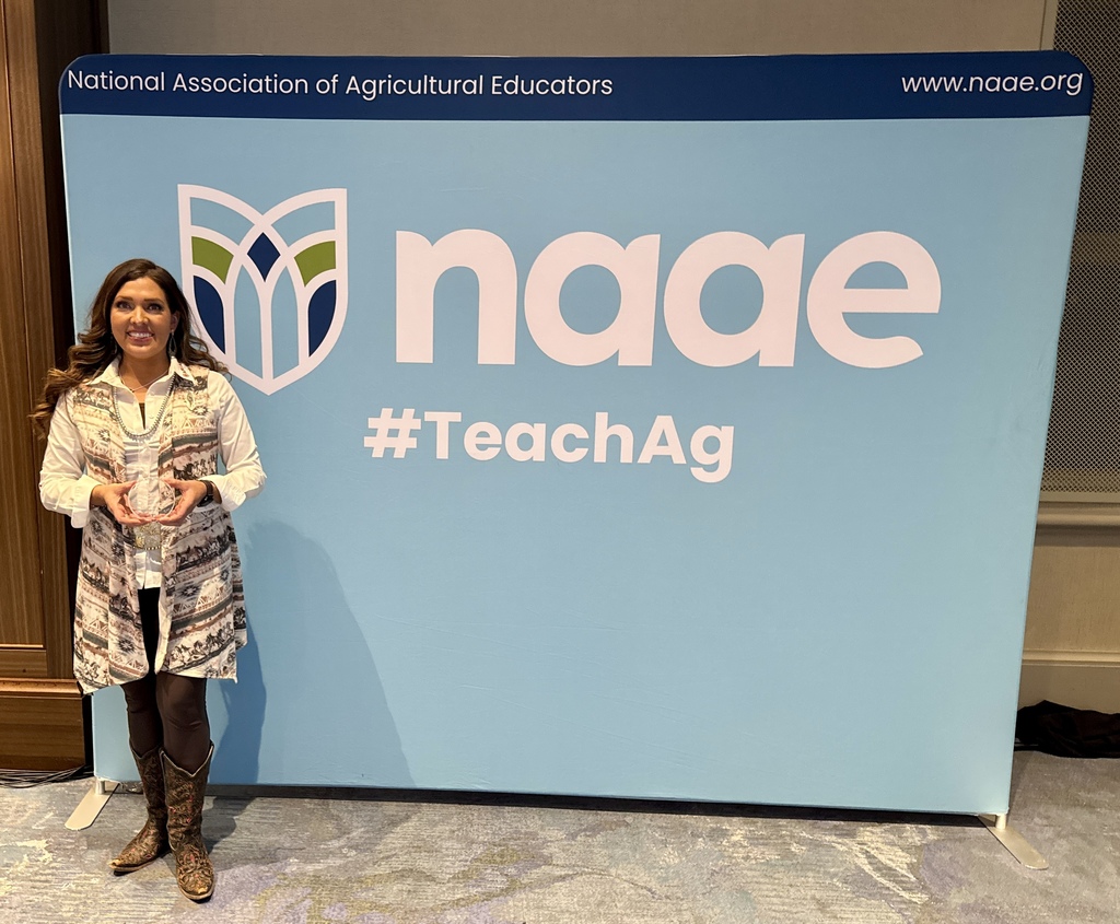 Lori Hoppe holds a small token, in front of the NAAE backdrop, for being a part of a profession program while at the NAAE convention.
