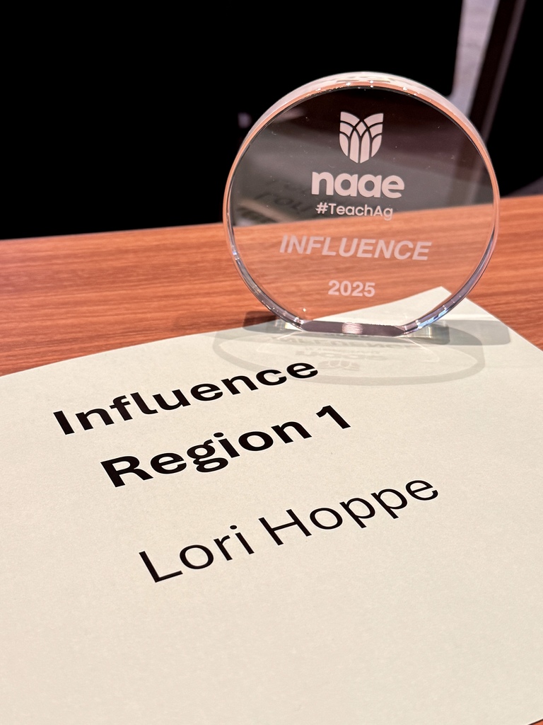 Image of the clear acrylic plaque saying NAAE Influence 2025 on top of a piece of paper that says Influence Region 1 Lori HOppe