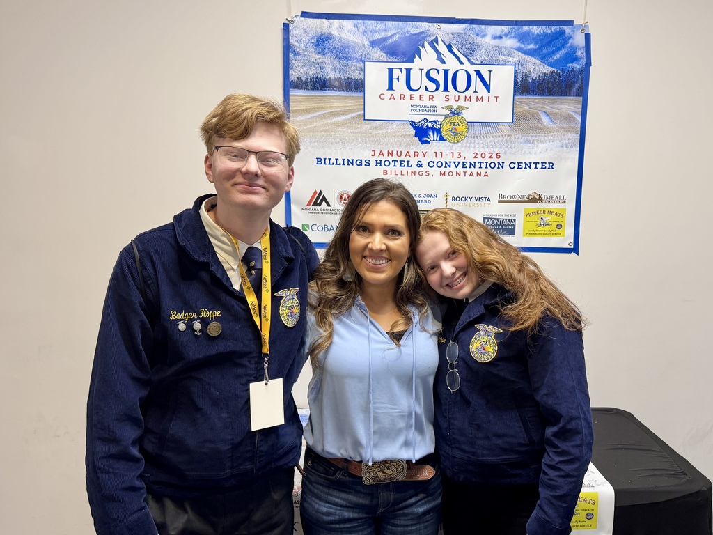 Two FFA members, in official dress, stand on each side of advisor Mrs. Hoppe while standing in front of the Fusion Career Summit banner.