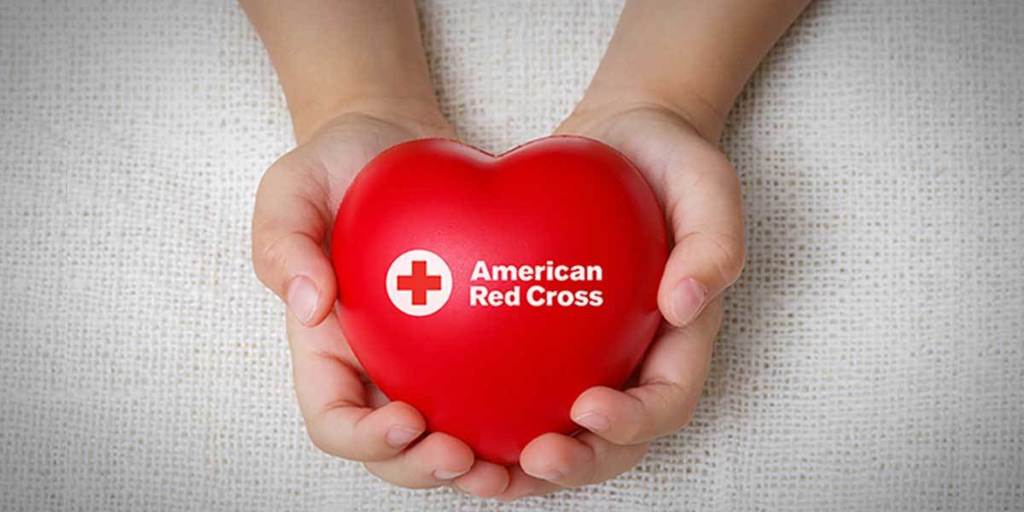 Two hands holding a plastic red heart that says American Red Cross