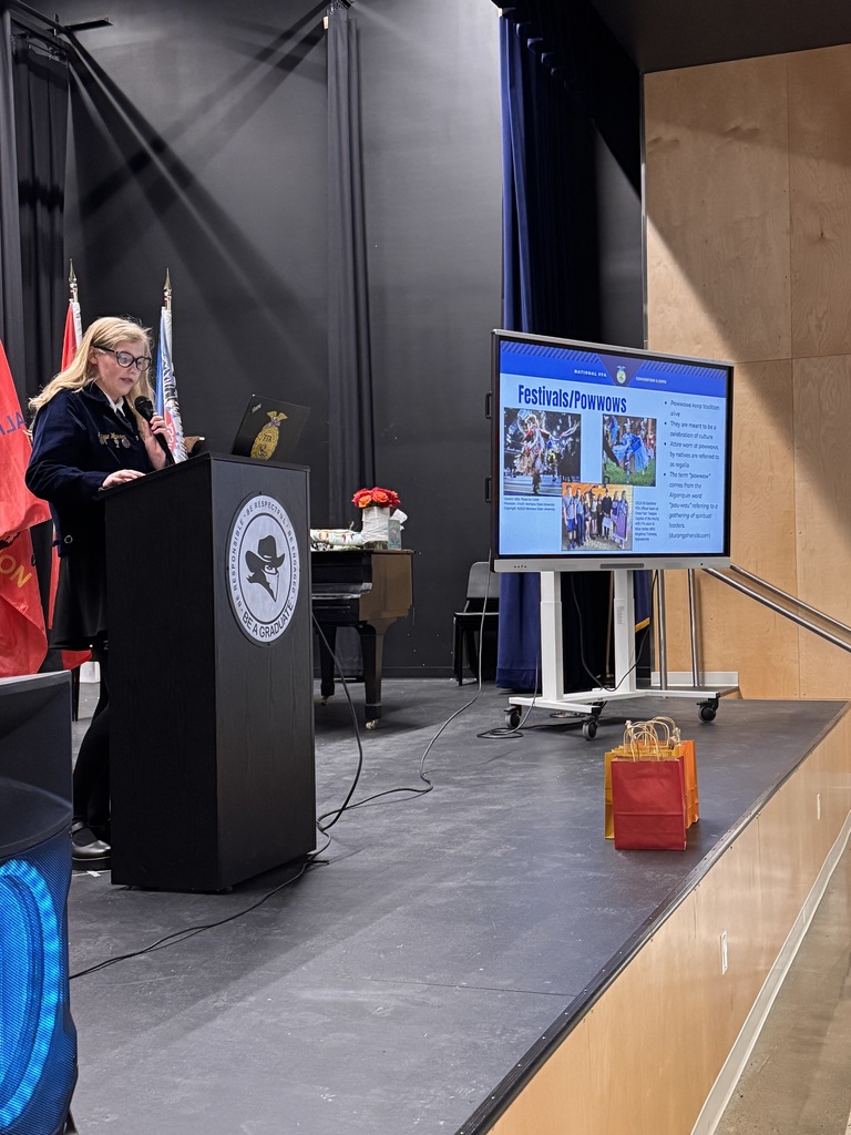 FFA member Maizie speaks into a microphone on a podium with a TV displaying a presentation on the side.