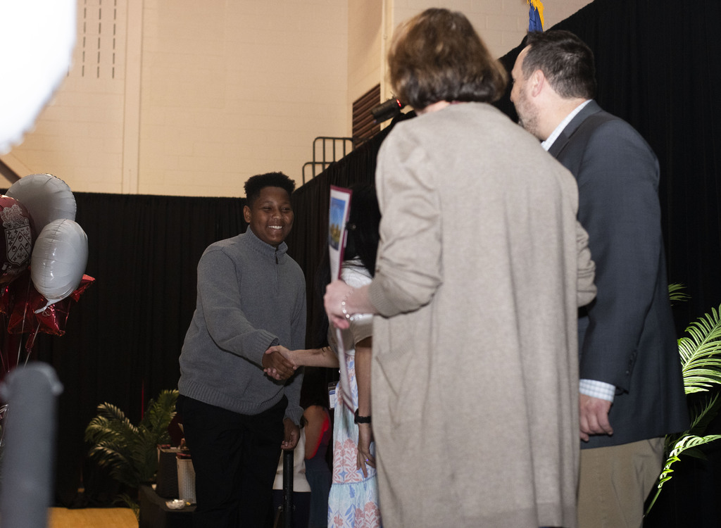 student smiling and shaking hands with faculty on stage receiving diploma