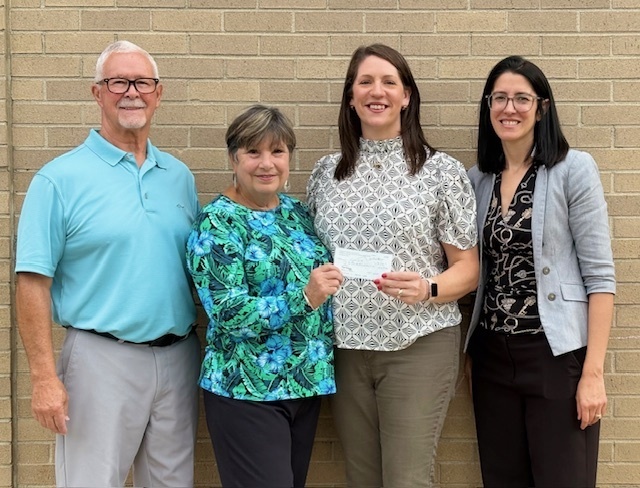 A picture of Mrs. Witt holding a check from the Andrew S. Woods Memorial Foundation, along with Chief Academic Officer Dr. Miller, and Mr. & Mrs. Woods.