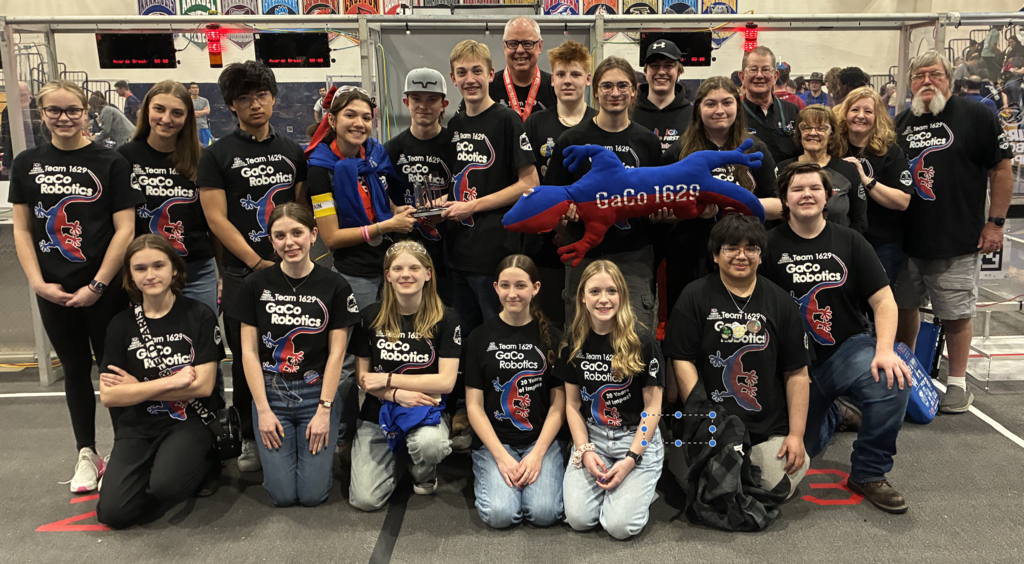 The entire robotics team poses together with their award, which is detailed in the text.