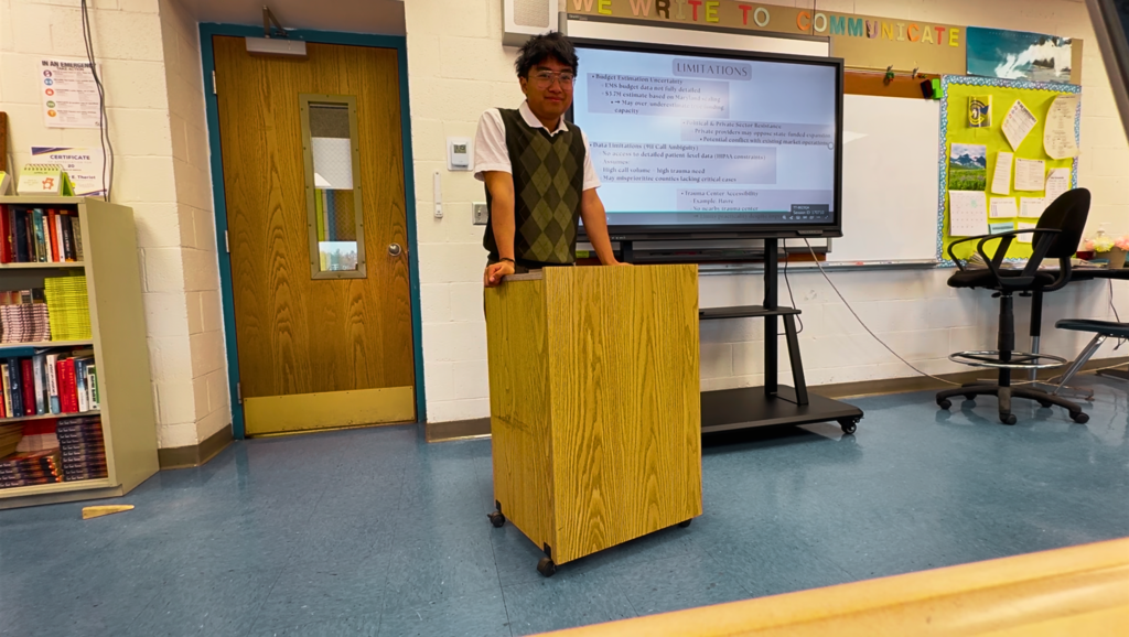 Image of a male student at a podium presenting on a screen.