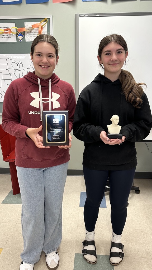 Two students pose for a picture, one holding a plaque and the other holding a trophy.