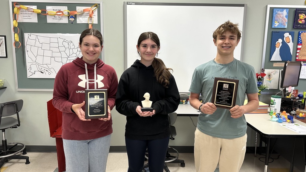 Three students pose together with their plaques and trophy.