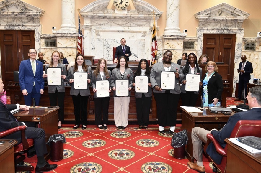 Image of student pages holding recognition certificates in the MD Captiol building.