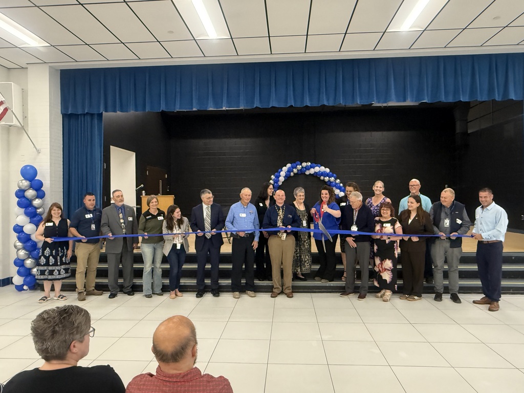 Representative from agencies involved with the Broad Ford School project stand in front of the stage about to cut the ribbon.