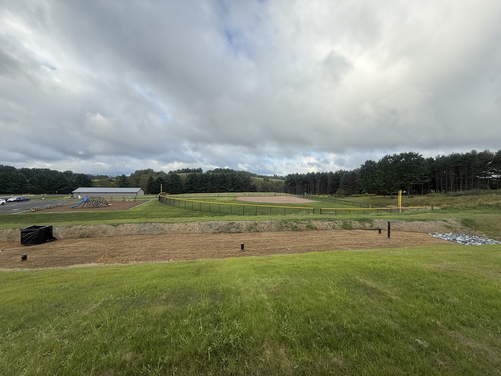 Image overlooking a storm water resevoir with a playground and ball field in the background.