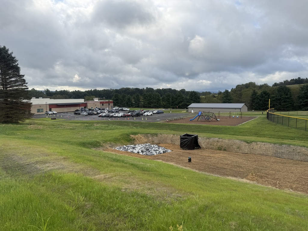An image containing a storm water resevoir, with a parking lot, playground, and school building in the background.