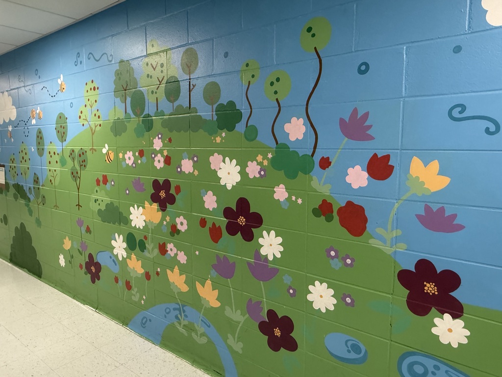 A mural is painted on a wall representing outdoor aspects of Crellin Elementary School. The mural represents the native flowers and plants on school campus.