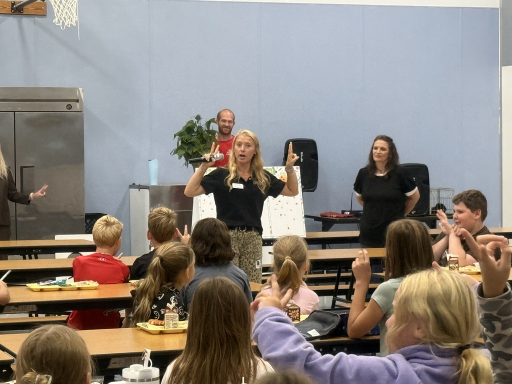 Image of Mrs. Mousch taking to students seated at their tables in the cafeteria.