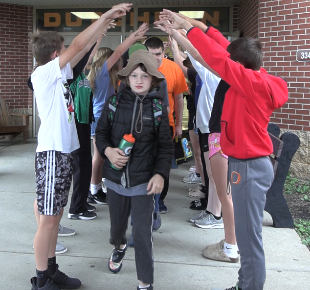 Students outside a building with brick walls. A group of them are raising hands.