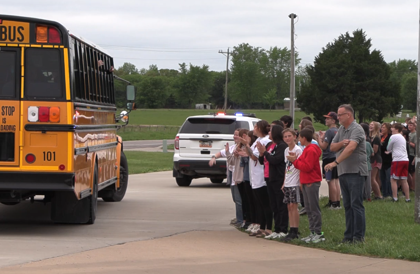A school bus is parked on the street with a crowd of people standing behind it.