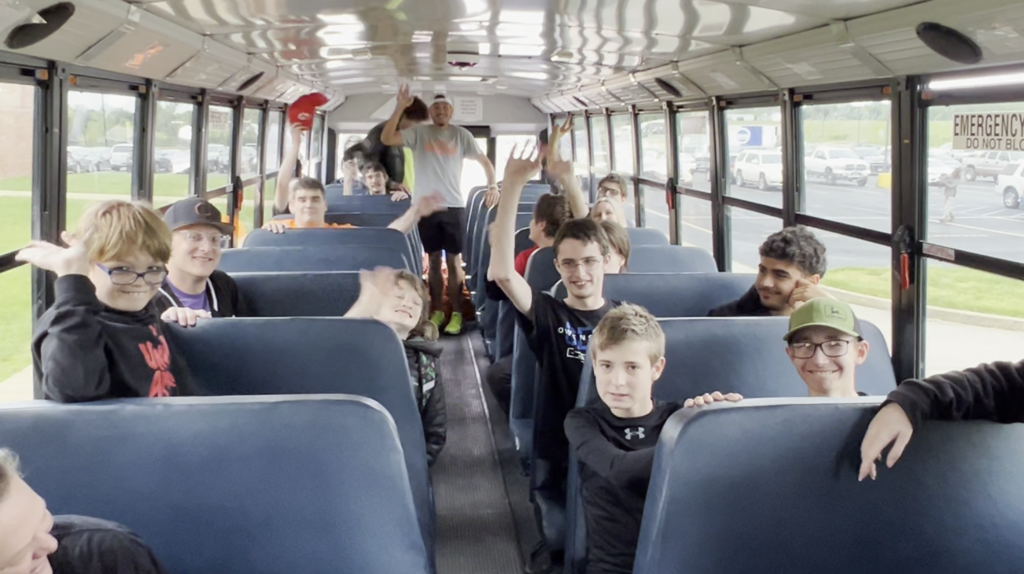 Interior of a school bus with several kids and two adults sitting on blue seats, looking around.