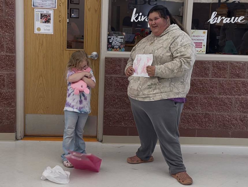 A woman holds a piece of paper, standing next to a girl in front of a building.