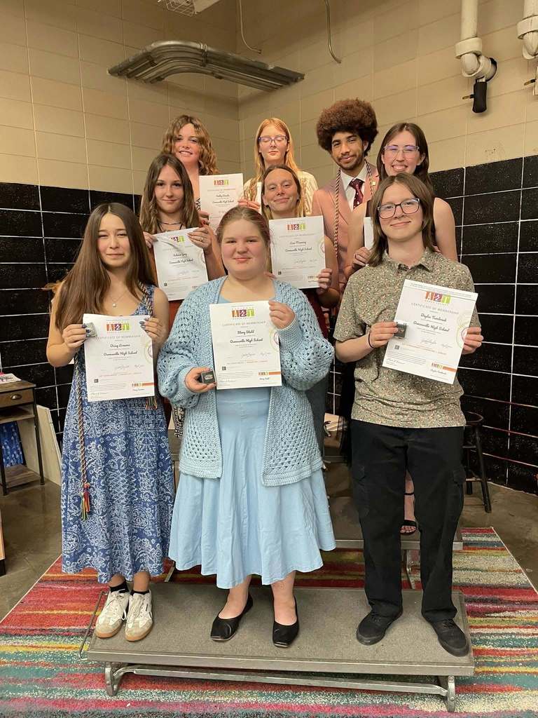 A group of students stand together, holding certificates, in a room with a tiled wall.