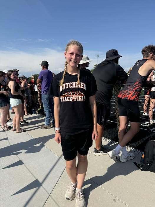 A woman in a black T-shirt and shorts stands outside, with several people around her.