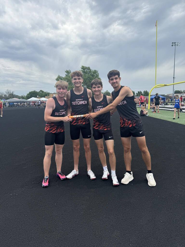 Four athletes in matching uniforms hold a baton between them on a track, with a cloudy sky and trees in the background.